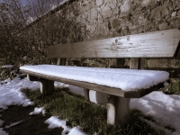 Sitzbank mit Schnee vor Mauer  im Sonnenlicht