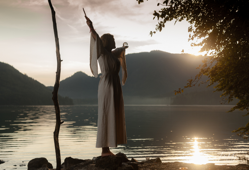 Mittelalterlich gekleidete Frau am Ufer des Walchensees im Sonnenaufgang