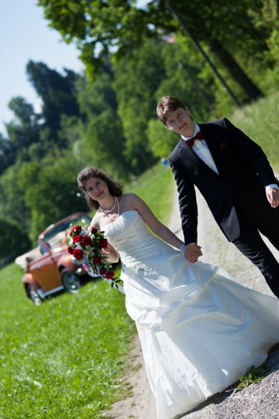 Brautpaar Händchen haltend auf Weg. Im Hintergrund Käfer Cabriolet