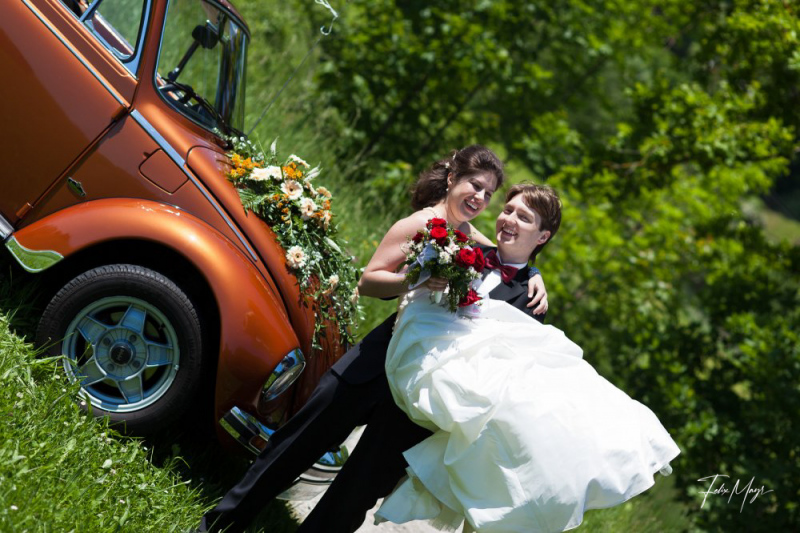 Bräutigam trägt Braut vor Käfer Cabriolet
