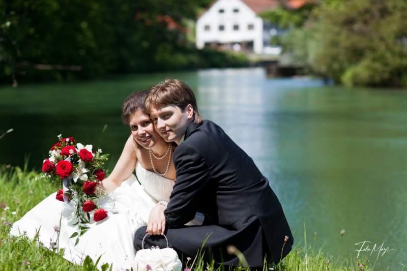 Brautpaar kniet in der Wiese vor einem Fluß