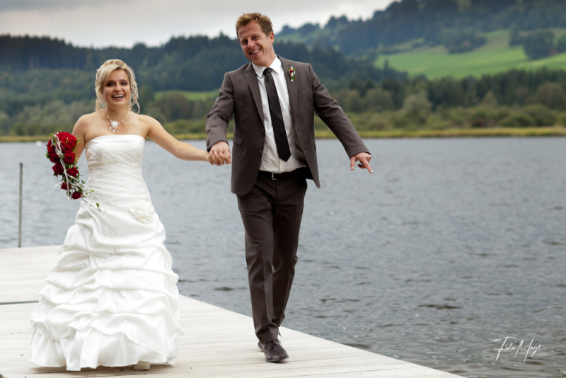 Brautpaar Händchen haltend auf einem Steg an einem See