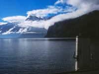 Blick über See mit wolkenverhangenen, schneebedeckten Bergen
