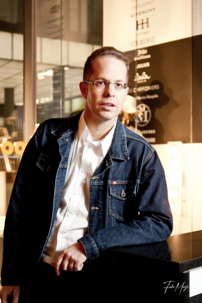 Mann mit Brille, weißem Hemd und Jeansjacke steh an Tresen